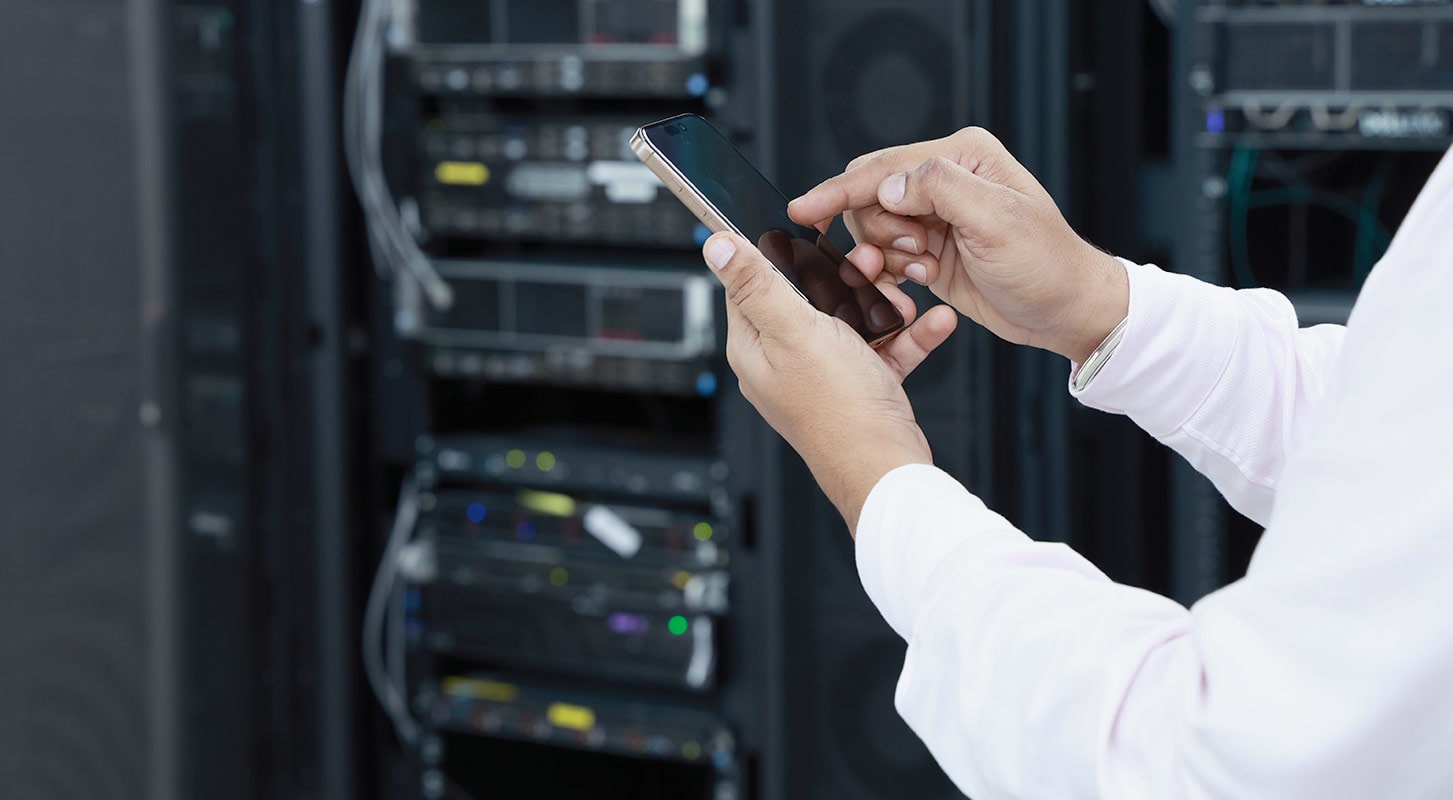 Individual with a cell phone stands before a server rack.